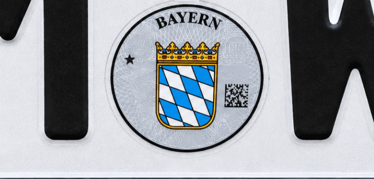 Ausschnitt eines Kennzeichens: Siegel mit QR-Code zwischen Ortskürzel und Buchstaben (Illustration)