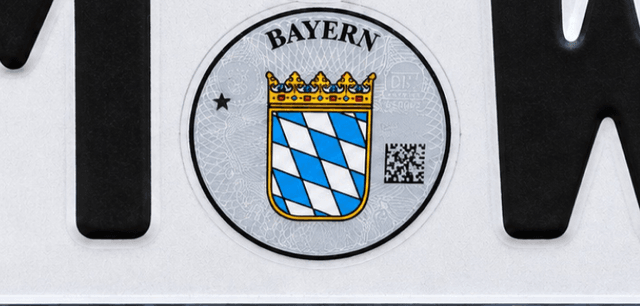 Ausschnitt eines Kennzeichens: Siegel mit QR-Code zwischen Ortskürzel und Buchstaben (Illustration)